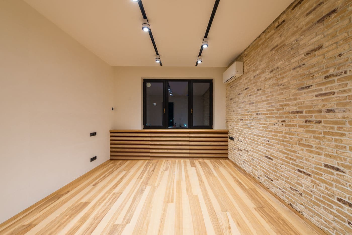 Empty room with track lighting, brick accent wall and wood floors